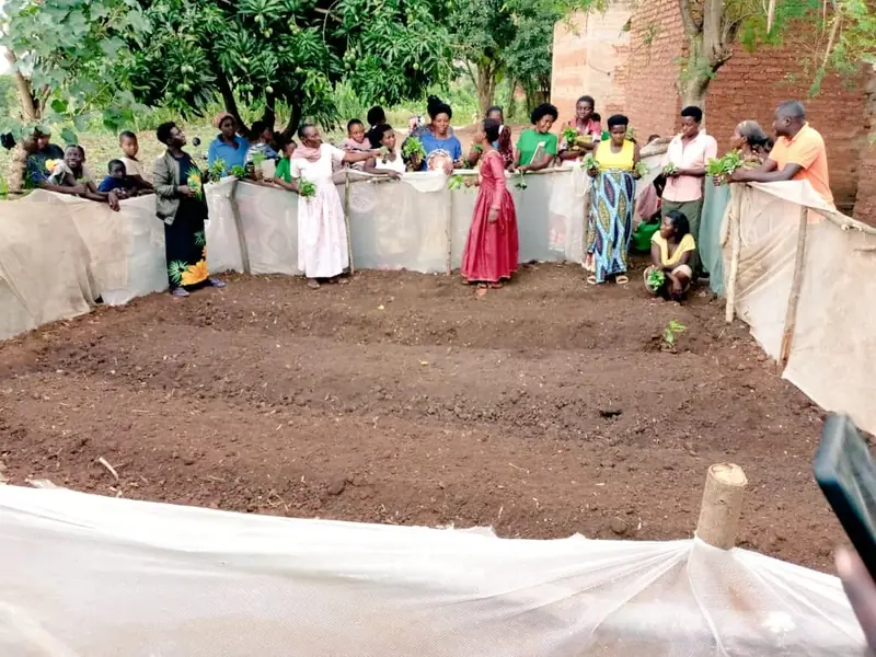 Community members stand around a prepared vegetable bed edged with sacking