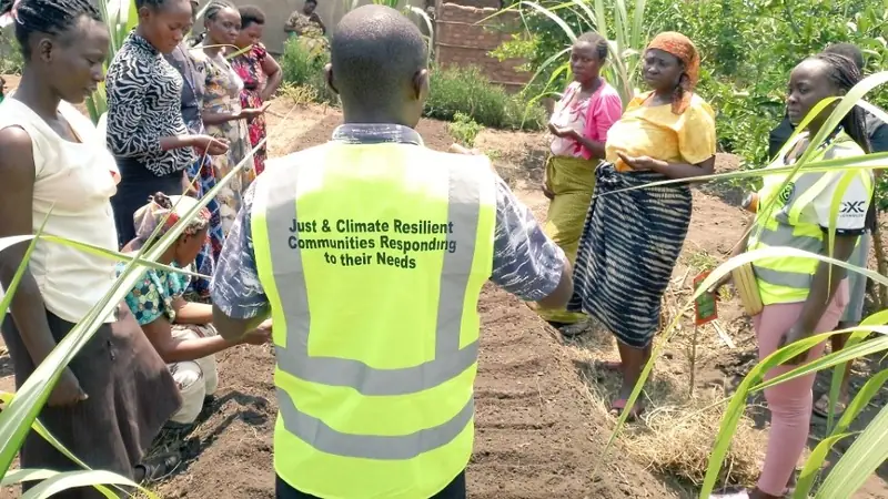 A Maru Foundation staff member in a vest talks with farmers beside a garden bed