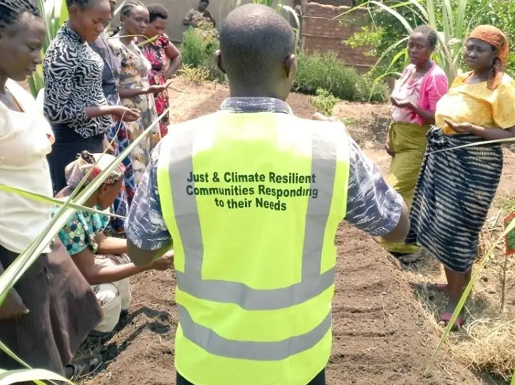 A man in a vest reading Just and Climate Resilient Communities works with farmers in a field