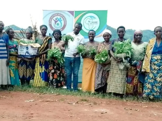 Women farmers hold bundles of seedlings in front of project banners