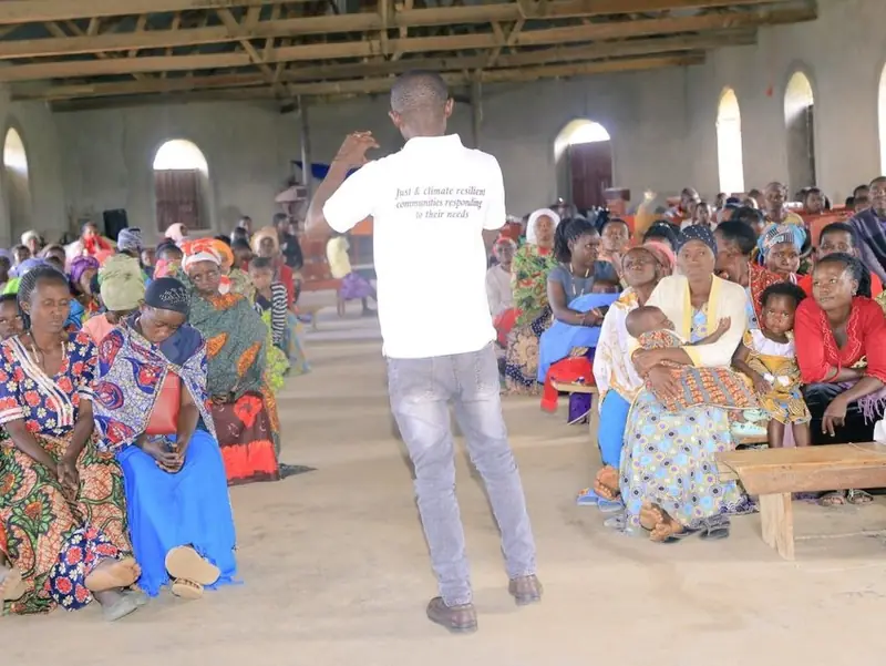 A facilitator addresses a large seated group inside a hall