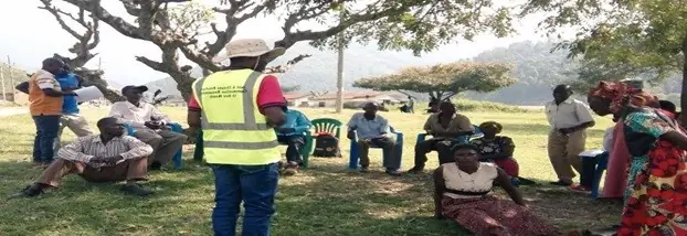 Community members gather outdoors under trees for an advocacy meeting