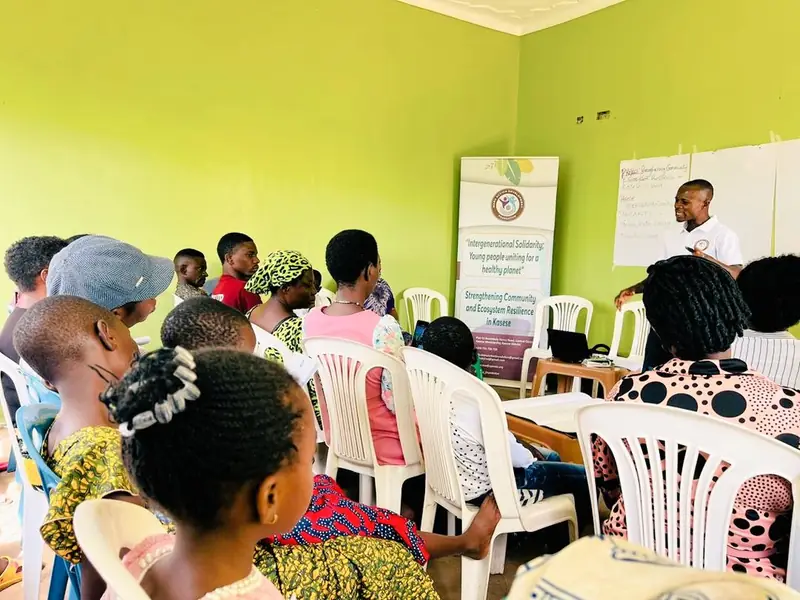 Young people seated in a training room listen to a session in front of project banners
