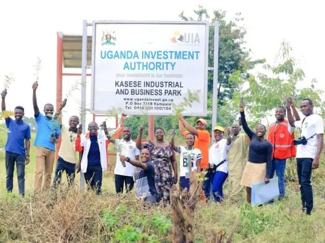 Participants raise their hands beside the Uganda Investment Authority Kasese Industrial and Business Park sign