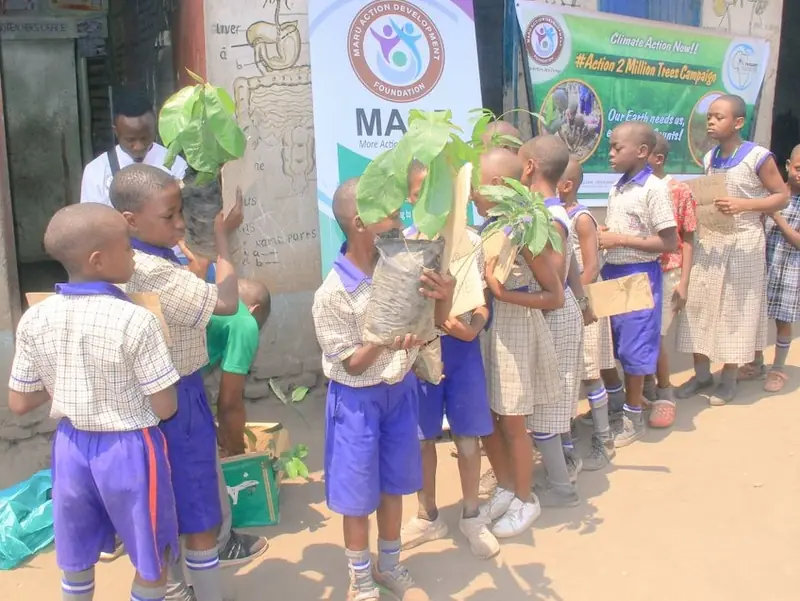 Pupils hold tree seedlings in front of a Maru Foundation banner