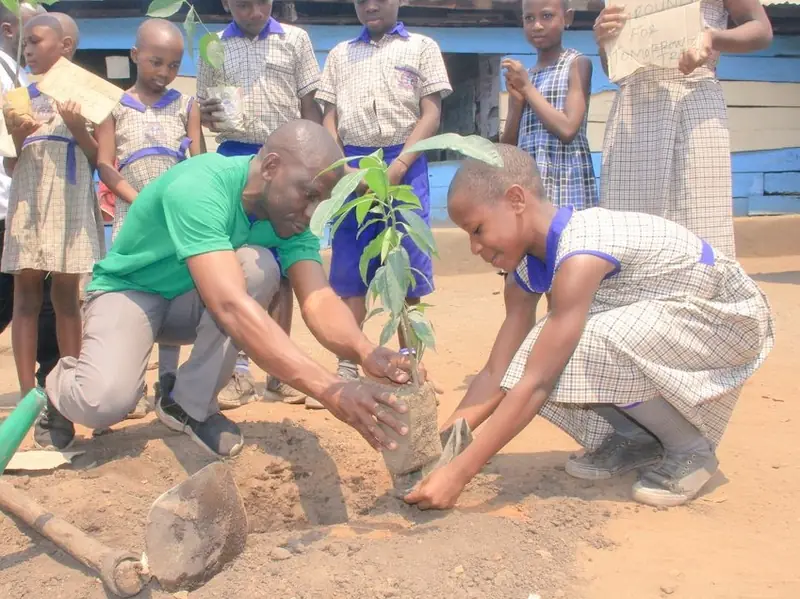 A volunteer and a pupil plant a tree seedling together