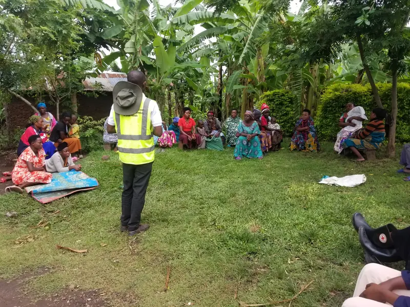 A facilitator in a high-visibility vest speaks to a seated community group