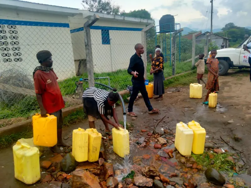 Children and adults collect water in yellow jerrycans at a school water point