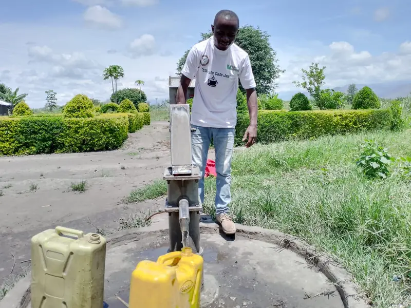 A man pumps water from a borehole while yellow jerrycans wait to be filled