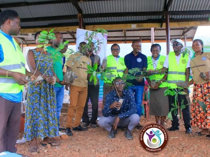 Community members and volunteers in vests hold seedlings for distribution