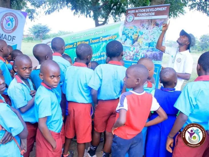 Pupils in blue uniforms gather to listen near a Maru Foundation banner