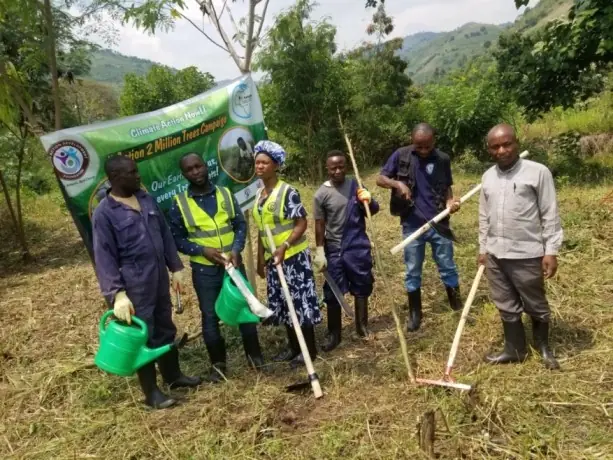 Volunteers with watering cans and hoes stand beside a Seeds of Resilience banner