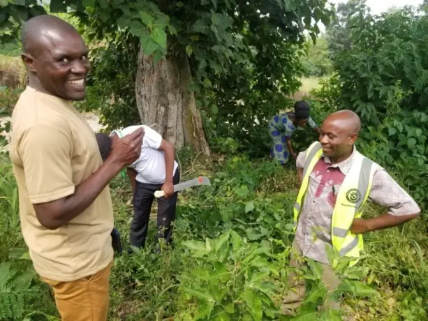 Two men smile while inspecting tree seedlings in a garden