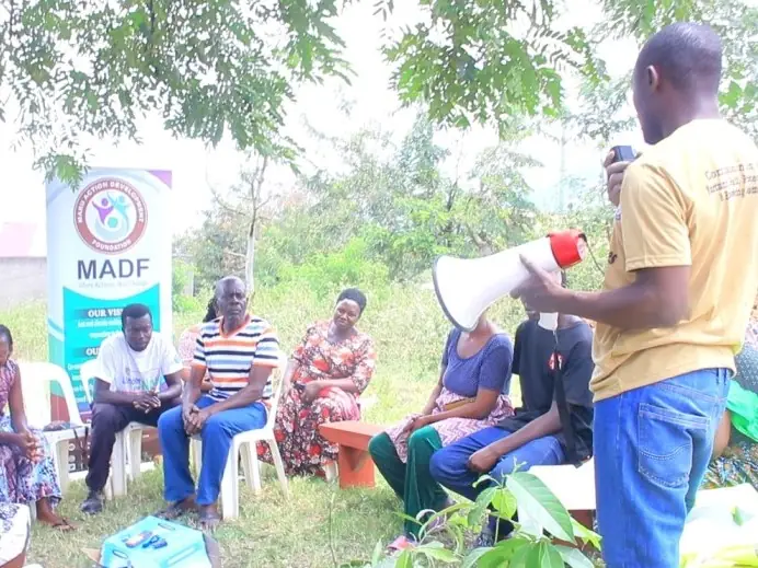 A facilitator speaks through a megaphone to a seated community group