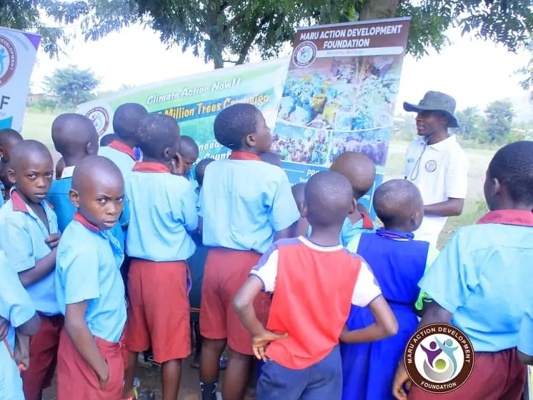 Pupils in uniform listen to a presentation in front of a project banner