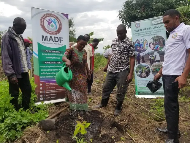 A woman waters a newly planted tree next to a Maru Foundation banner